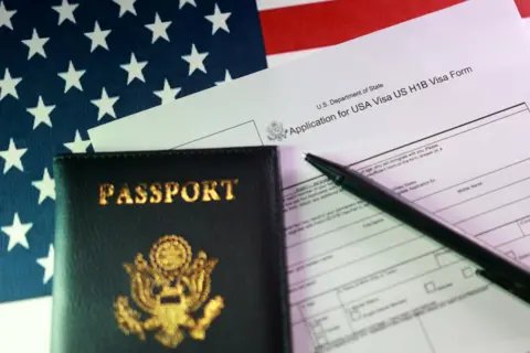 Reuters An application for an H-1B visa sits on a table alongside a US passport, a pen and an American flag. 