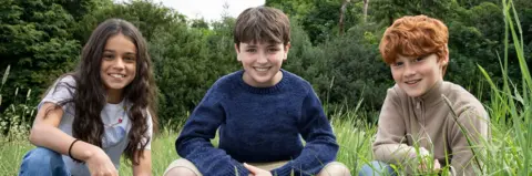 HBO Arabella Stanton, Dominic McLaughlin and Alastair Stout smiling while crouching in a field