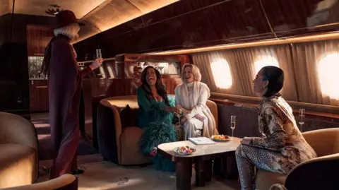 Disney+ Naomi Watts, Niecy Nash, Glenn Close and Kim Kardashian pictured in new Disney+ show. They are all sitting on a private plane, drinking champagne.